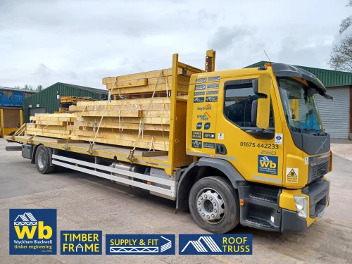 Yellow Wyckham Blackwell branded lorry carrying roof trusses on a cloudy day.