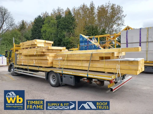 Yellow Wyckham Blackwell branded lorry carrying roof trusses on a cloudy day.