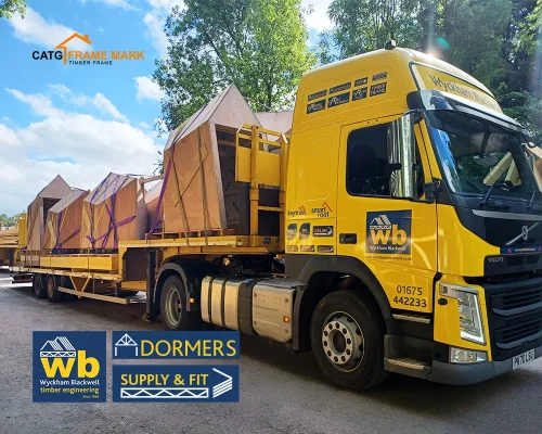 Yellow Wyckham Blackwell flatbed truck carrying pre-built timber Dormers.