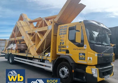 Yellow Wyckham Blackwell flatbed truck carrying large prefabricated timber roof trusses.