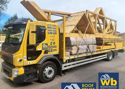 Yellow Wyckham Blackwell flatbed truck carrying large prefabricated timber roof trusses.