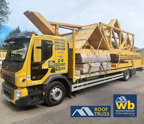 Yellow Wyckham Blackwell flatbed truck carrying large prefabricated timber roof trusses.