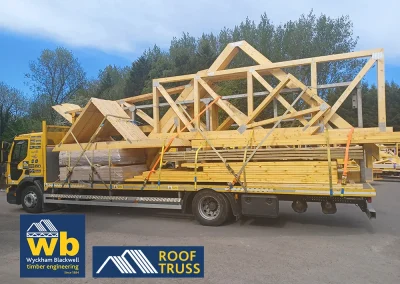 Yellow Wyckham Blackwell flatbed truck carrying large prefabricated timber roof trusses.