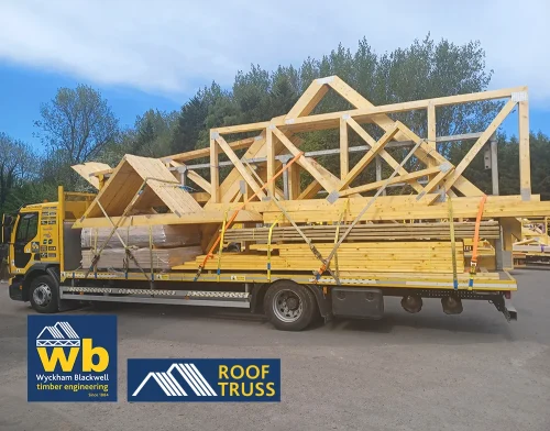 Yellow Wyckham Blackwell flatbed truck carrying large prefabricated timber roof trusses.