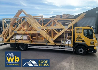 Yellow Wyckham Blackwell flatbed truck carrying large prefabricated timber roof trusses.