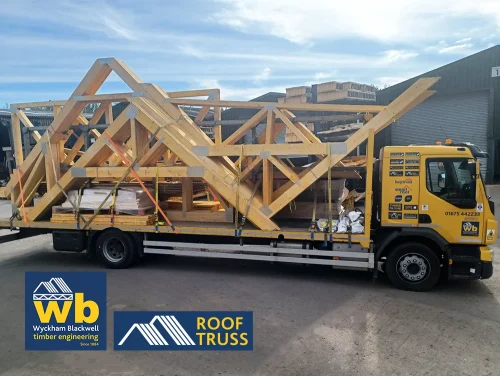 Yellow Wyckham Blackwell flatbed truck carrying large prefabricated timber roof trusses.