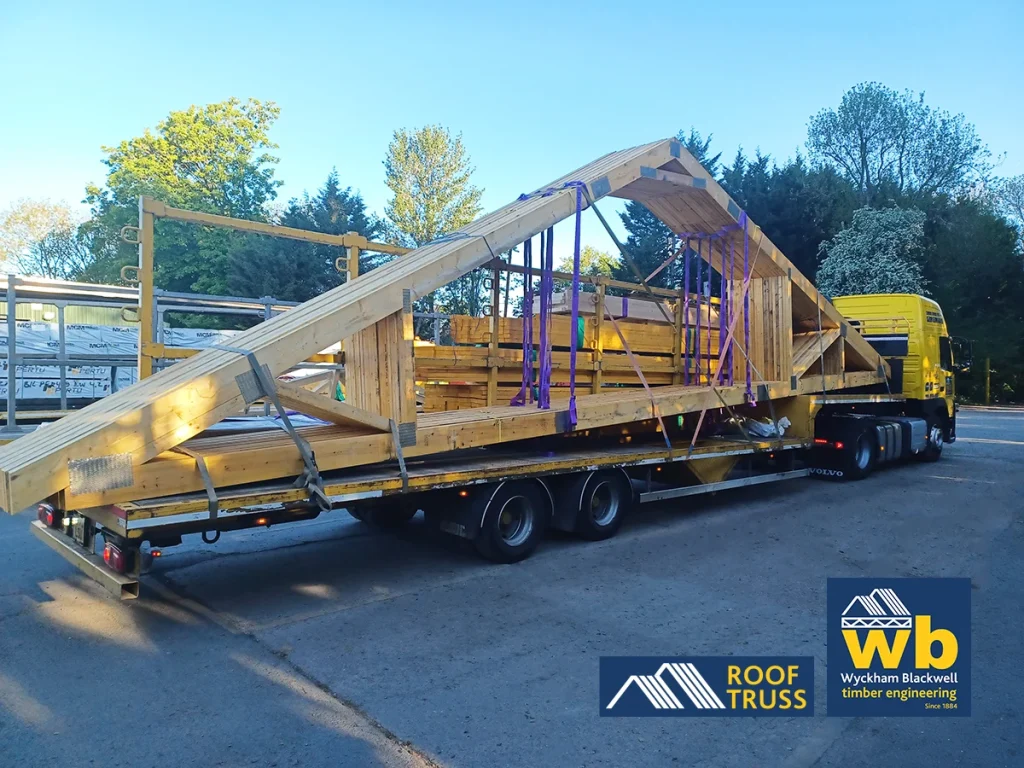 Large wooden Roof Trusses strapped on a yellow Wyckham Blackwell flatbed truck.