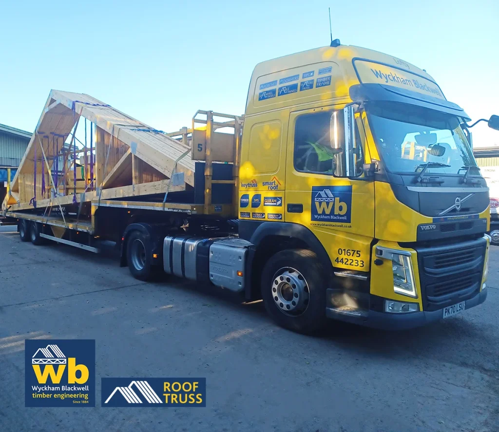 Large wooden Roof Trusses strapped on a yellow Wyckham Blackwell flatbed truck.