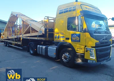 Large wooden Roof Trusses strapped on a yellow Wyckham Blackwell flatbed truck.