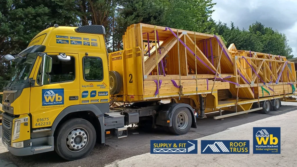 Yellow Wyckham Blackwell lorry hauling stacked wooden roof trusses secured with purple straps on a roadside.