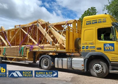 Wyckham Blackwell yellow lorry loaded with stacked wooden roof trusses secured by purple straps.