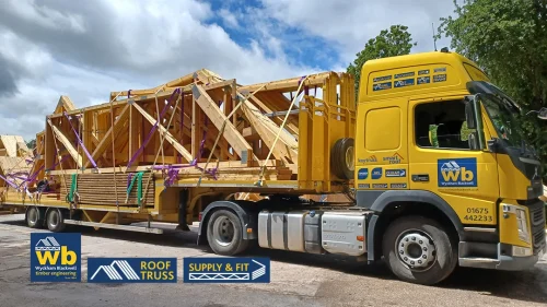 Wyckham Blackwell yellow lorry loaded with stacked wooden roof trusses secured by purple straps.