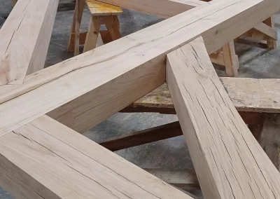 Large oak timber feature truss with intersecting beams resting on sawhorses in a workshop, Wyckham Blackwell logo in bottom right.