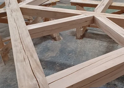 Large oak timber feature truss with intersecting beams resting on sawhorses in a workshop, Wyckham Blackwell logo in bottom right.