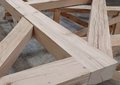 Large oak timber feature truss with intersecting beams resting on sawhorses in a workshop, Wyckham Blackwell logo in bottom right.