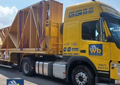Yellow Wyckham Blackwell truck hauling wooden roof trusses on a flatbed trailer.