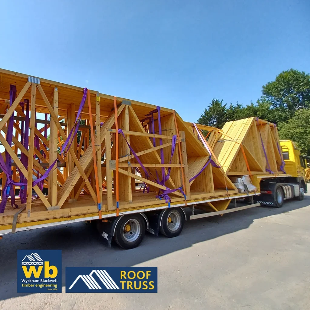 Yellow Wyckham Blackwell truck hauling wooden roof trusses on a flatbed trailer.