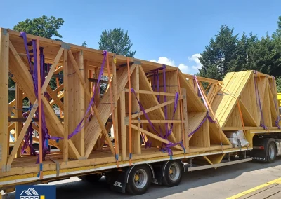 Yellow Wyckham Blackwell truck hauling wooden roof trusses on a flatbed trailer.