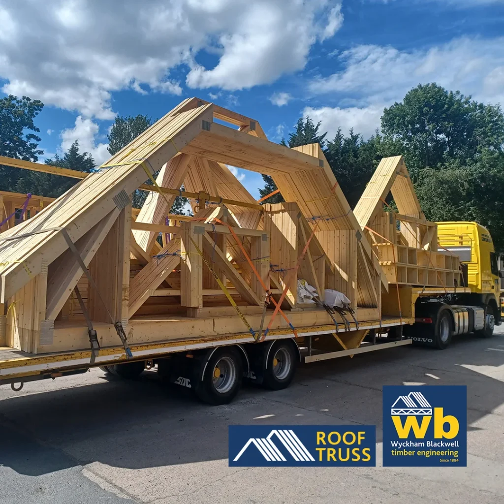 Wyckham Blackwell flatbed truck loaded with large prefabricated wooden roof trusses under blue sky.