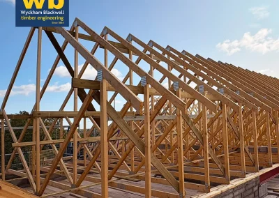 Rows of timber Roof Trusses on a building frame under a blue sky, with Wyckham Blackwell logos above.