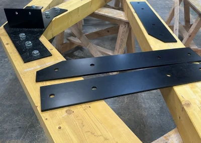 Glulam Feature Truss assembly on sawhorses with black steel connector plates and bolts in workshop; Wyckham Blackwell logo at bottom.