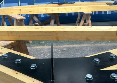 Glulam Feature Truss beams with bolted black steel connector plate in workshop, Wyckham Blackwell logo bottom left.