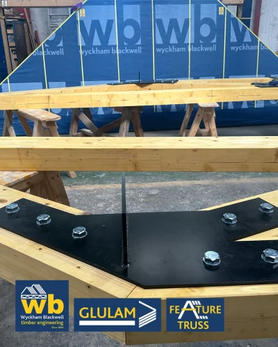 Glulam Feature Truss beams with bolted black steel connector plate in workshop, Wyckham Blackwell logo bottom left.